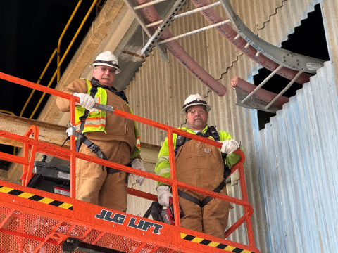 Two employees stand on a raised platform and perform electrical work