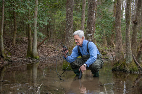 A man crouches down in water and uses a device to test it