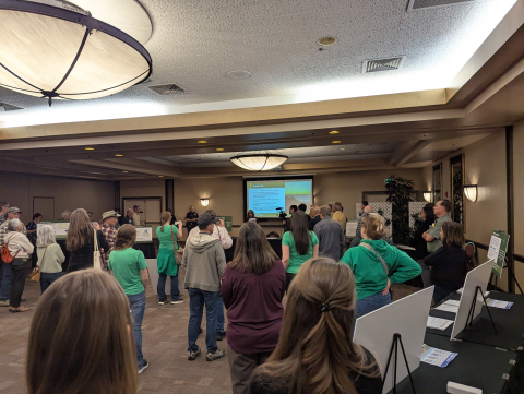 A group of people in a room face the front of the room where a presentation is being given