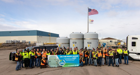 Large group of employees standing around a truck with large tanks of waste on it