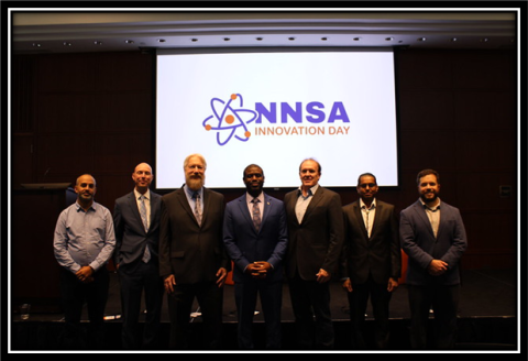Seven Men stand in front of an NNSA Innovation Day Logo