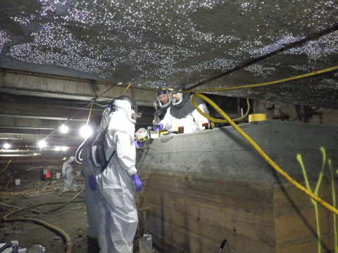 Workers in safety gear perform tasks in the basement of a complex
