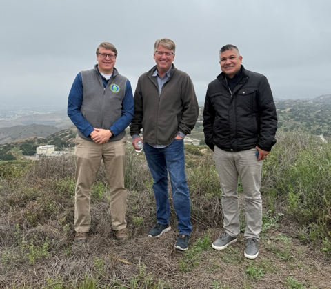 Three men stand outside in front of foggy mountains and valleys