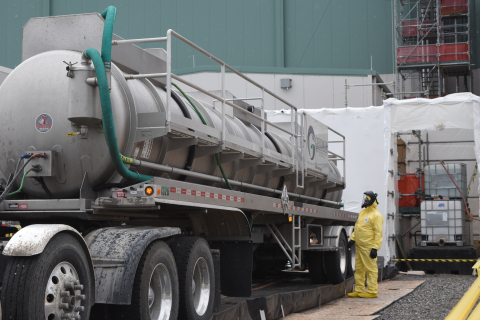 A large tank truck parked with an employee in a hazmat suit standing beside it