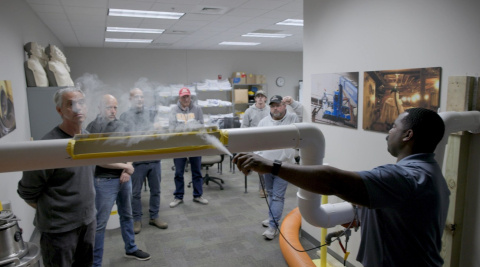 A man spraying a white substance onto a pipe while other employees watch