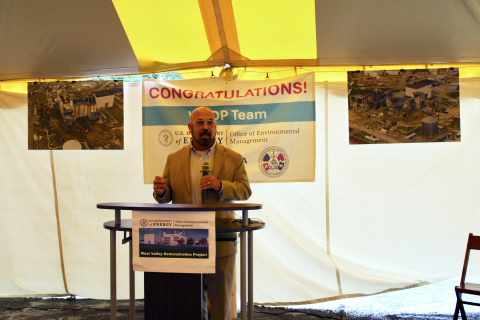 A DOE-EM Leader (male) on a stage standing behind a podium