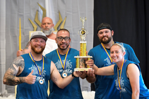 A group of four people in blue shirts posing for a photo and holding up a trophy