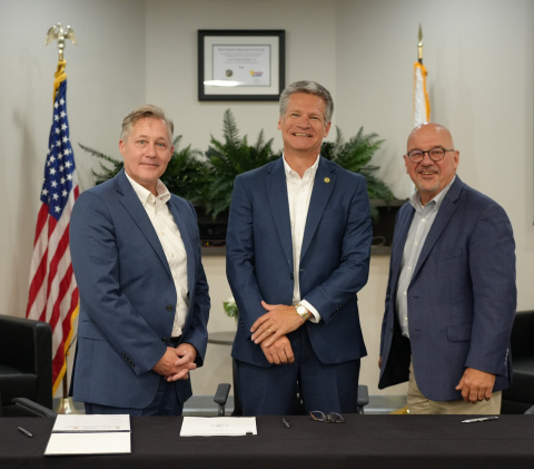 Three men in an office smile for a group photo