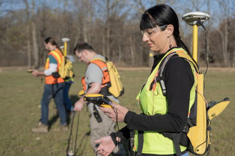 Three employees surveying land while wearing protective gear