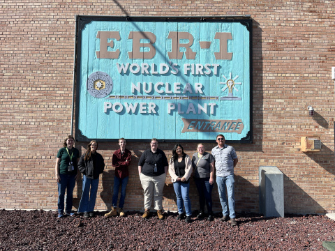 A group of interns posing for a picture in front of a light blue sign on a brick wall