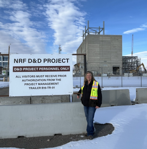 A woman in a yellow and orange safety vest standing beside a sign outside of a laboratory building 