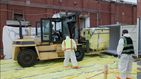 Employees in protective gear using a construction vehicle to clear out a site