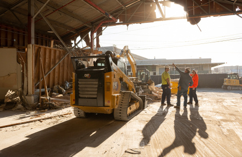 A construction vehicle outside with a few employees standing beside it