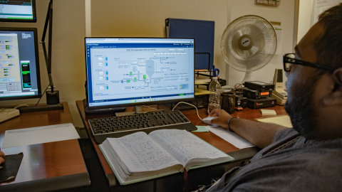 A worker sitting in front of a computer with a book open in front of him as well