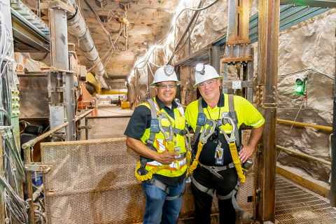 Two men in yellow safety vests and white hard hats pose for a picture inside the Waste Isolation Pilot Plant 