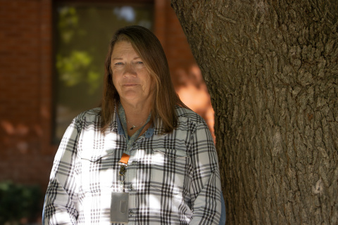 A woman in a plaid shirt standing beside a tree smiling for the picture