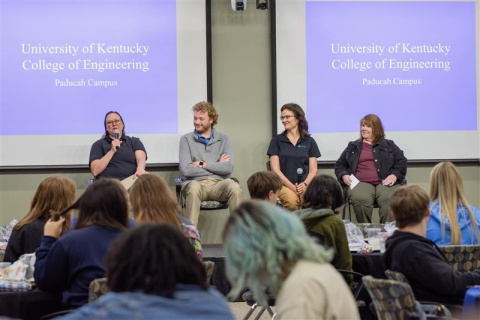 Four individuals sitting on stage participating in a panel in front of an audience