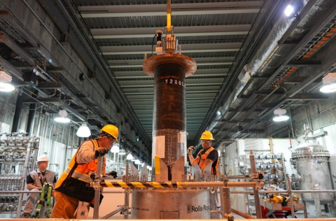 Employees in protective gear standing beside a large flow filter inside a facility building