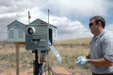 A man outside at the Hanford site working on an air monitor