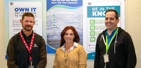 A group of three professionals posing for a group photo in front of educational posters