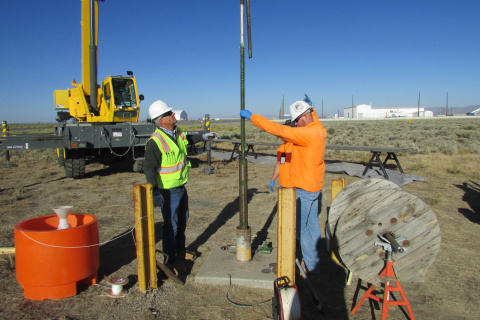 Two employees in protective gear working on a groundwater pump outside at the Idaho National Laboratory