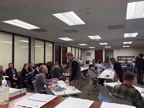 A room full of professionals, some sitting at tables and some standing in a room