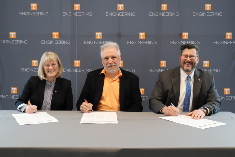 Three professionals sitting at a table smiling for a picture while signing a piece of paper