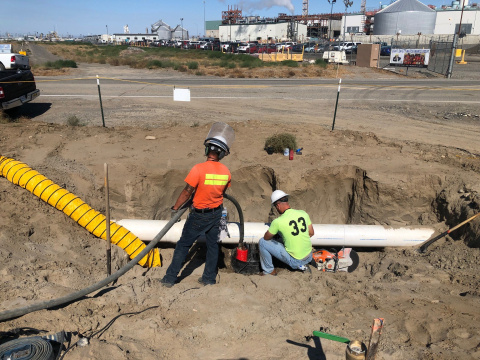Employees in protective gear working in a trench on a white pipe