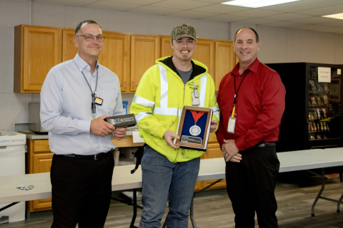 Three professionals posing for a picture, the one in the middle holds an award