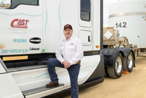 A man in a white shirt, blue jeans and black hat standing beside a large white truck