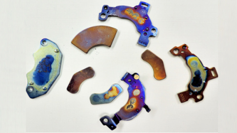 A photo of four voice coil magnets taken from a desktop or laptop computer and their brackets (which have mounting holes). These magnets are each about 10.5 - 15 grams, 1 - 1.25 inches long. These ones are colorful, because they have been overheated in the process of separation and demagnetization.