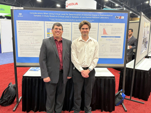 A intern and mentor smile for a picture in front of a poster at a conference