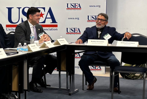 Two people wearing suits and ties sitting near each other on adjacent desks.