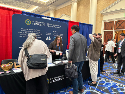 People talking at a conference booth with a large banner behind them about the Office of Indian Energy.
