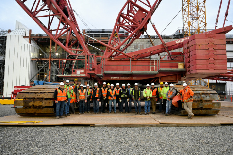 A group of workers in protective gear pose for a photo in front of a large crane