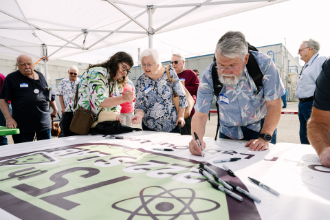 Attendees at a 75th Anniversary for the Hanford 222-S Lab sign a paper with the logo