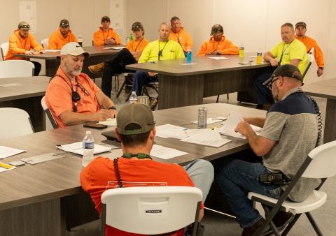A group of employees sitting at tables in a room while wearing neon yellow and orange shirts