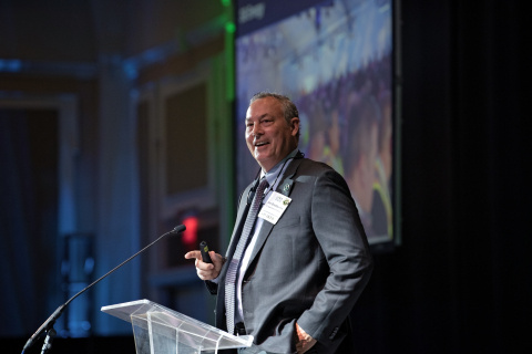 A man in a suit giving a key note address at a conference standing behind a podium