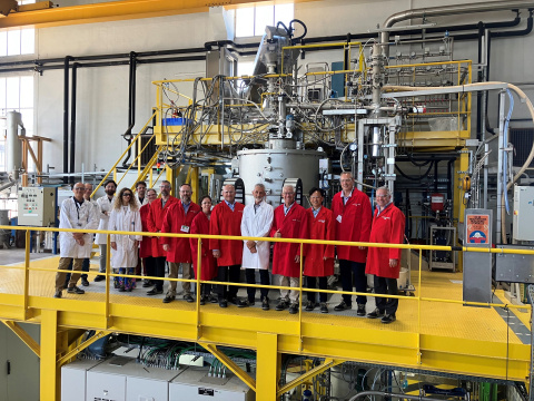 A group of DOE and French leadership in red and white lab coats in a large lab