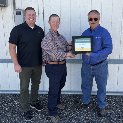 Three professionals smile for a group photo, two of them holding an award certificate