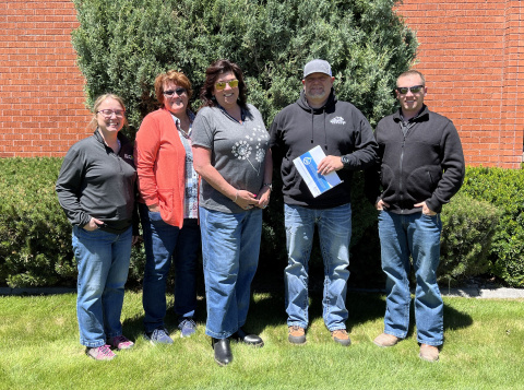 A group of five Idaho Site employees posing for a picture outside in front of a brick building 