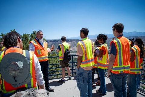 A group of students touring the Los Alamos Site wearing yellow and orange safety vests