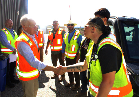 A group of DOE employees and leadership in yellow and orange safety vests touring the Los Alamos site, two people shake hands in the foreground