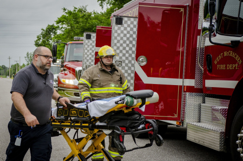 Two emergency responders pushing a gurney during a training drill, they are walking beside a firetruck