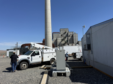 A white pickup truck outside of a building at the Hanford Site with employees installing a large wireless antenna