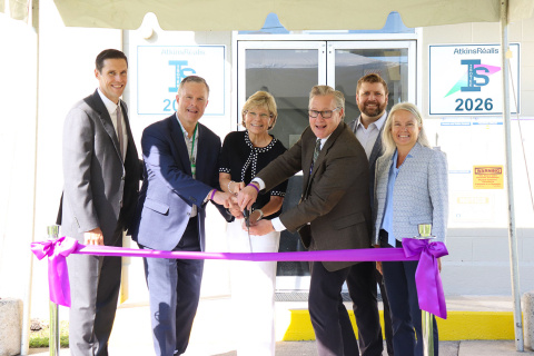 A group of professionals conducting a ribbon cutting in front of a building with a purple ribbon tied in front of them