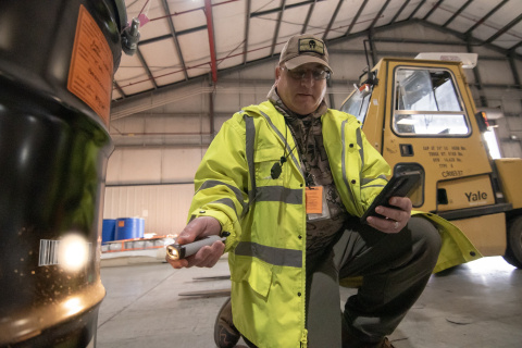 A man in a yellow jacket using a barcode scanner on the side of a black container