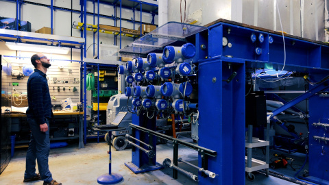 A researcher at Argonne National Laboratory stands next to a large equipment assembly painted blue.