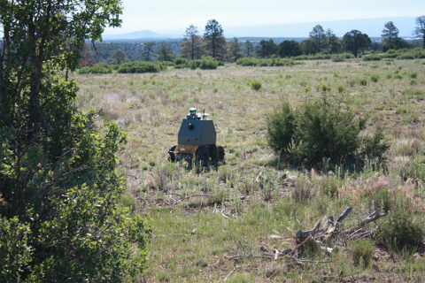 A grey robot with wheels on grass at the Los Alamos site