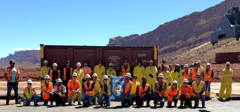 A large group of people wearing yellow and orange safety tear and white safety hats pose for a picture